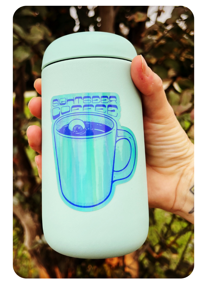 An image showing a blue Sightseer coffee mug holographic sticker, set on a light blue travel mug and a hand holding it.